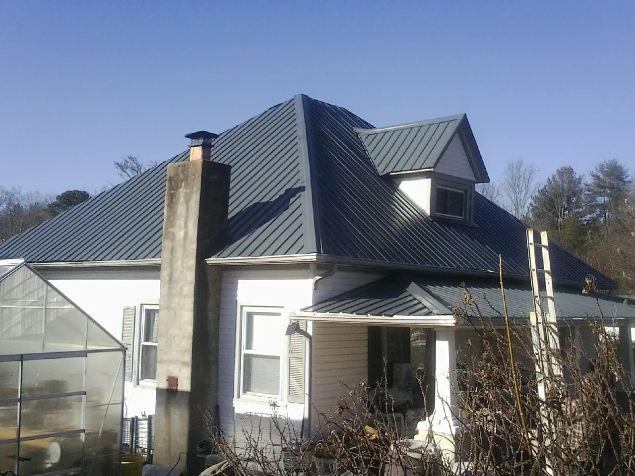 Dark blue standing seam metal roof on a white farmhouse with dormer — Slate & Tile Roof Repair by Roofing Brothers in Corunna