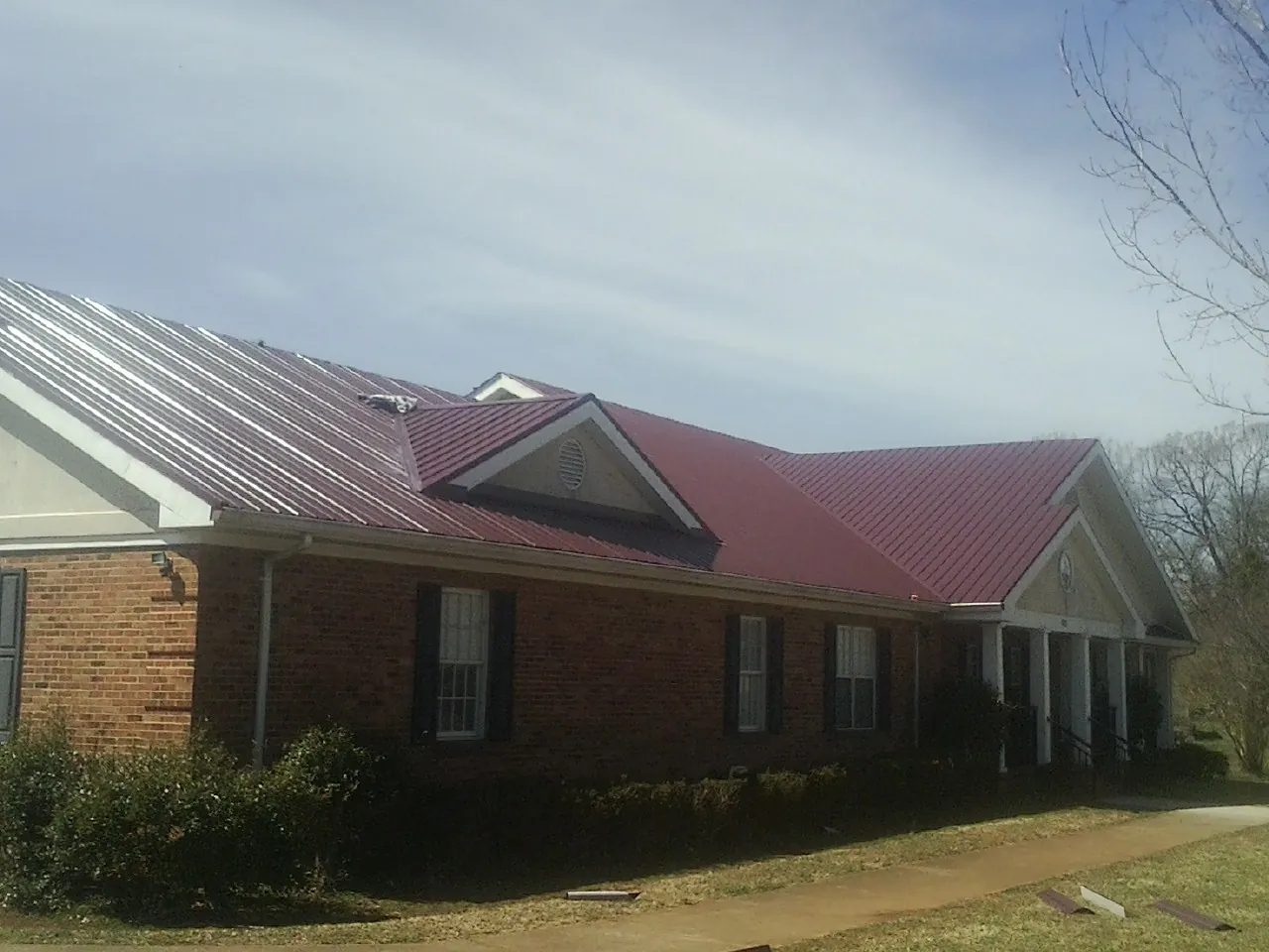 Red metal roof with gabled entries on a long brick building, from a Hail Damage Roof Repair job in Corunna