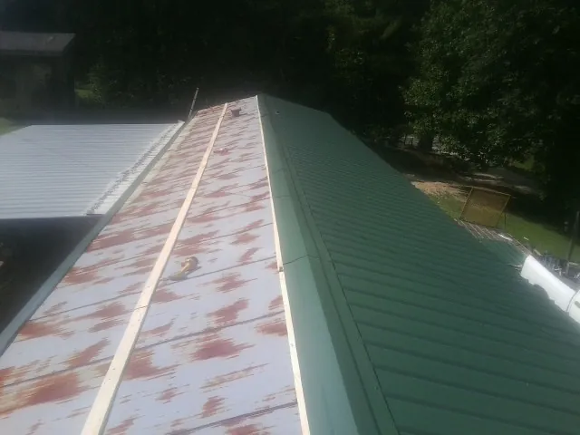 Old rusted panels beside newly installed green metal roofing — Wind Damage Roof Repair by Roofing Brothers in Corunna